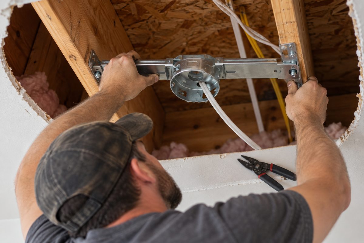Expanding steel junction box brace fitted between wooden joists for ceiling fan installation